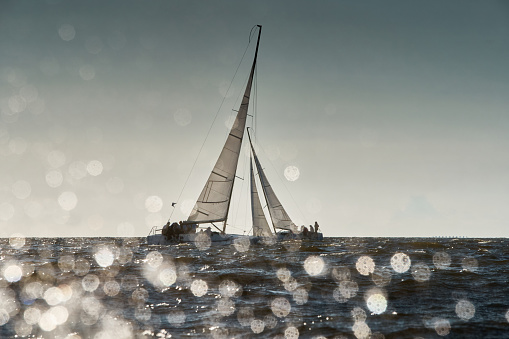The view through the spray of how the two sailboats are heeling at sunset, boat roll, splashes shine in the sun, sailors on the boards. High quality photo