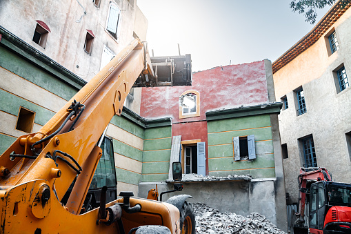 Close-up of a colorful building being demolished by construction machinery. This photo was taken from the street in France.
