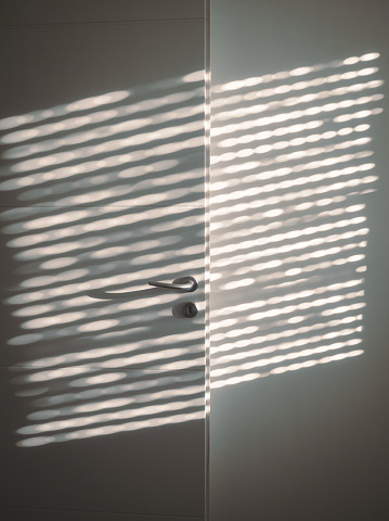 Rays of the sun penetrating inside a dark room, through window blinds in summer.