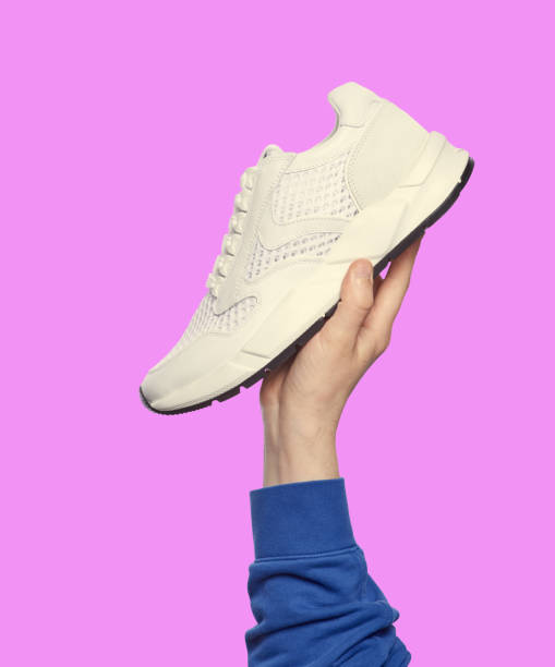 istock Man's hand holding a modern white sneaker isolated on a lilac background. Sport and active lifestyle. Footwear sales advertising campaign 1601345830