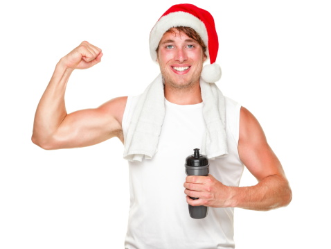 Christmas fitness man showing bicep muscles fit for holidays. Handsome male in his 20s wearing santa hat isolated on white background.Fitness athlete man portrait- Young muscular sporty fit caucasian man isolated on white background.