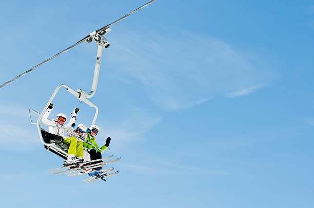 Trio of skiers riding on a ski lift Happy skiers on ski lift - space for text ski lift stock pictures, royalty-free photos & images