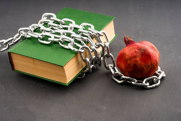 a green book is chained on a gray background and a pomegranate fruit