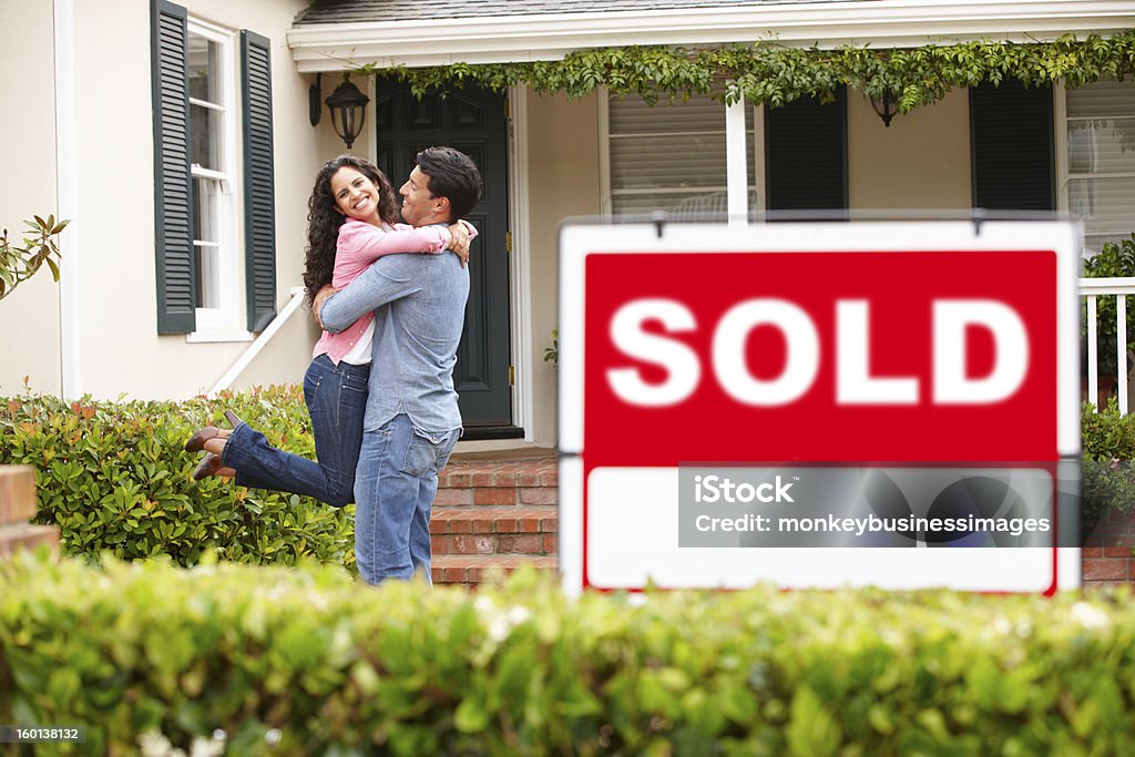 Hispanic couple outside home with sold sign Happy hispanic couple hugging outside home with sold sign Sold - Single Word Stock Photo