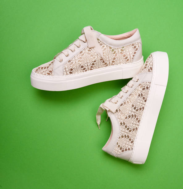 istock Trendy comfortable beige knitted design sneakers with white thick rubber soles and wide shoelaces, isolated on a bright green background.  Summer season footwear concept 1601387875