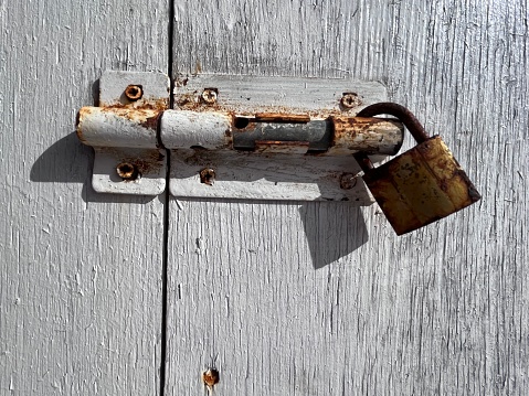 Old faded brown padlock and chain on an old weathered wooden gate.