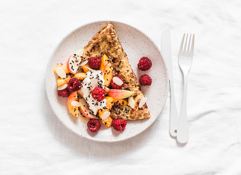 Oatmeal pancake made of whole grain flakes and eggs with fruits, berries and Greek yogurt on a light background, top view