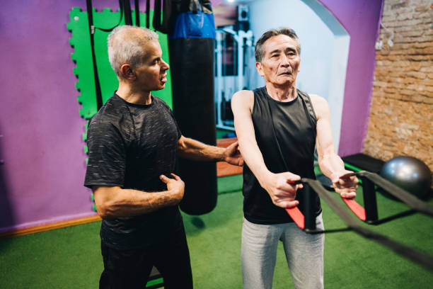 istock Personal trainer assisting senior man exercising using TRX at the gym 1601421578