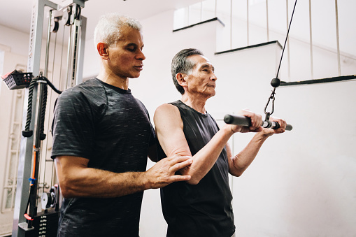 Personal trainer helping senior man training at the gym