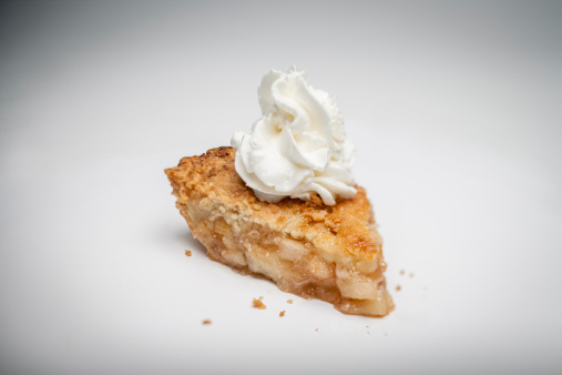 A studio photo of apple pie (pastry dessert)  with whipped cream on top taken with a selective focus or shallow depth of field.