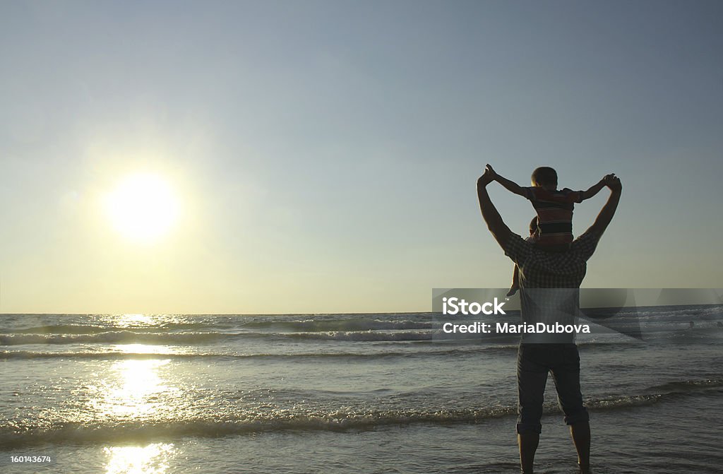 Father with son on shoulders at the beach  Father and son taking a walk on the sea. sunset. Child Stock Photo