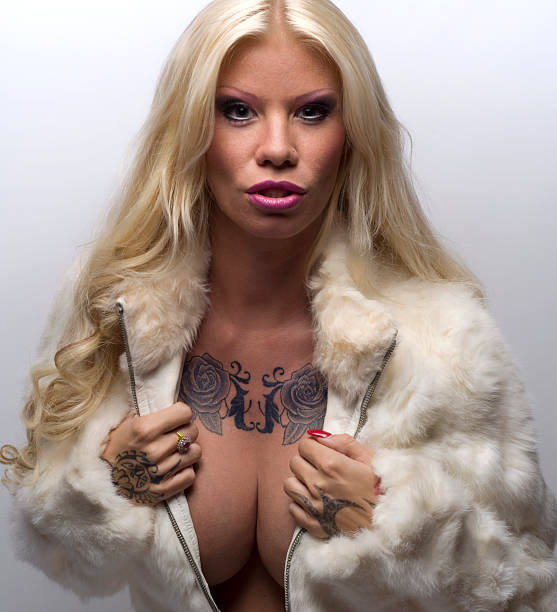 Beautiful Long Hair Tattoo Blonde In Fur Coat And Breasts Beautiful Long Hair Tattoo Blonde In Fur Coat And Breasts and cleavage and a chest tattoo. black pin up girl tattoos stock pictures, royalty-free photos & images