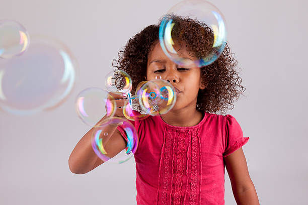 poco chica asiática africana soplando burbujas de jabón - bubble child bubble wand blowing fotografías e imágenes de stock