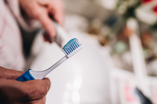 Close-up of a woman putting toothpaste on toothbrush in the bathroom at home