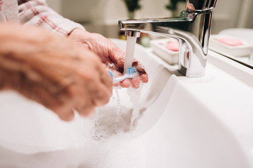 Close-up of a senior washing toothbrush in the bathroom