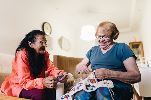 Senior friends talking and crocheting at home
