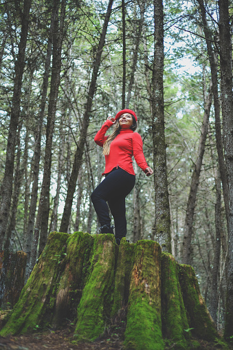 Woman with positive attitude on a mossy tree stump in the middle of the forest.
