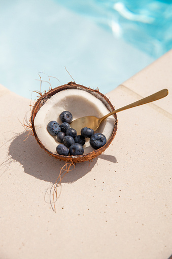 Fresh fruit next to swimming pool with Coconut half and blueberries healthy snack