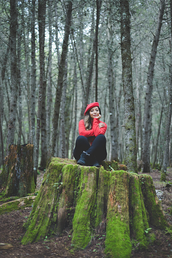 Woman in a calm and thoughtful attitude on a mossy stump in the middle of the forest.