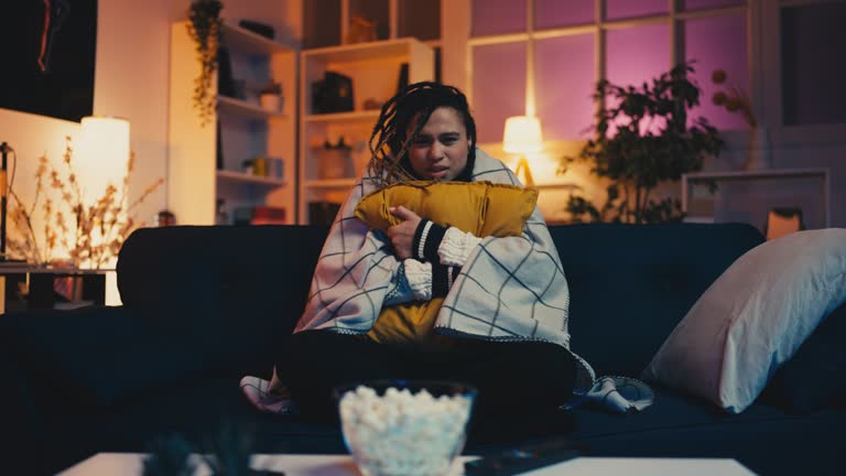 Young African American woman watching horror movie at home, entertainment