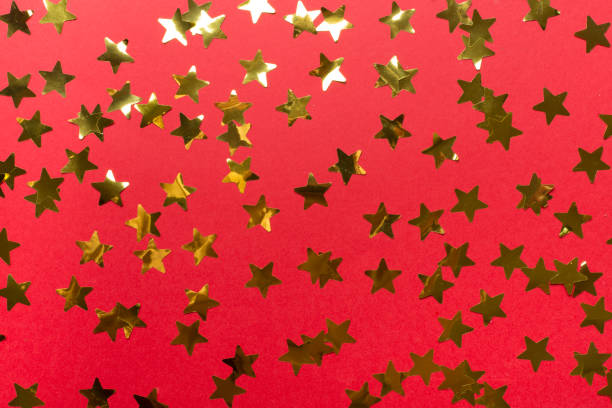 Golden confetti stars on color background, top view.