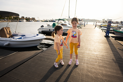 Two little girls playing together on a pier in a sunny summer day.