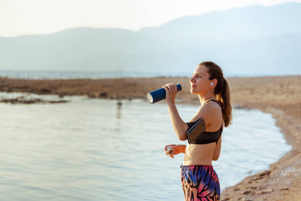 istock Young woman drinking water on the beach after run 1601589340