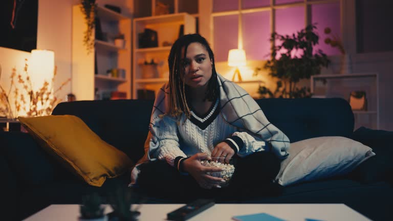 Stylish African American woman watching thriller film and eating popcorn at home