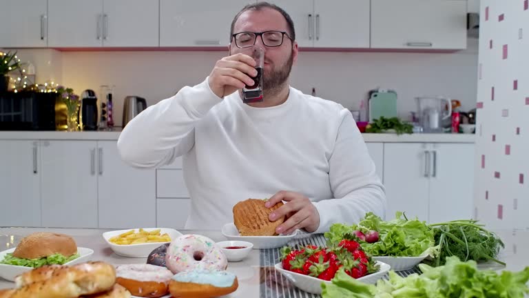 Fat man eating a cheeseburger and fast food meal with a drink.