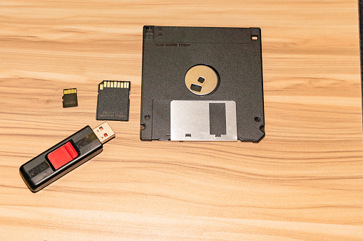 Two dusty stacks of obsolete computer disks in transparent plastic CD cases and audio recording cassettes from the 1990s and 1980s.