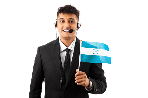 Young hispanic call center agent man business suit holding honduras flag looking positive and happy standing and smiling with a confident smile showing teeth