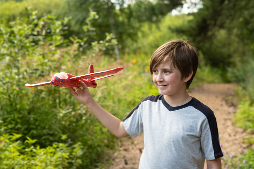 happy boy playing with a toy plane in the park. joyful 10 year old child holds a red plane in his hands, plays with it in nature during the summer holidays, on a sunny day.
