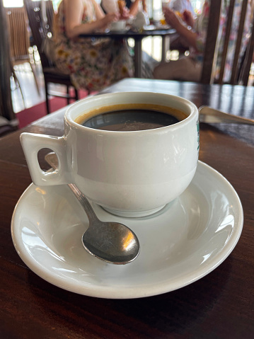 Stock photo showing a freshly made, hot cup of coffee, pictured on a wooden table and ready to drink.  The black Americano coffee is presented in a simple, white china cup and saucer.