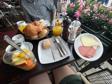 Stock photo showing close-up, elevated view of restaurant continental breakfast meal of white plate with, ham, salami and cheese, stainless steel basket containing Italian white bread rolls and cornetti (croissants) glasses of orange juice and glasses of fruit salad.