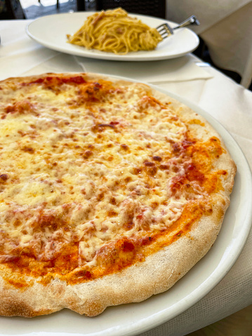 Stock photo showing close-up view of white plates, one with Pizza Margherita and another with a portion of spaghetti carbonara, using a traditional Italian recipe.