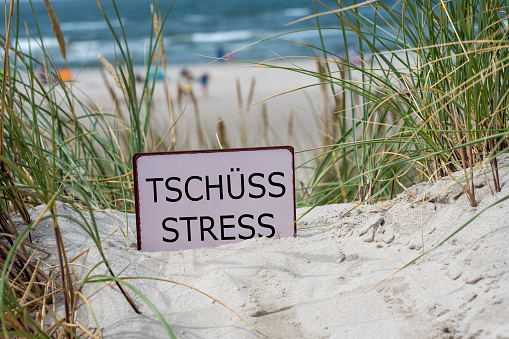 The German text 'Tschuess Stress' (goodbye stress) in the sand dunes at the beach.
