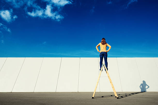 Overcome adversity Woman on top of folding ladder looks across a wall. a frame ladder pictures stock pictures, royalty-free photos & images