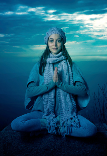 Young woman meditating in nature sitting on the rock.