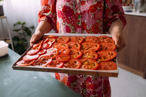 A close up view of an unrecognizable Caucasian female holding a tray with tomato slices while making a healthy vegetarian meal in the kitchen.