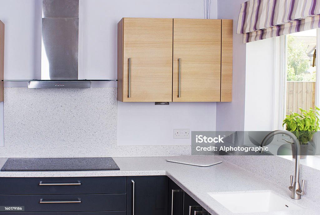 Modern kitchen State of the art domestic kitchen with hi gloss grey cupboards and oak cabinets and induction hob, set in a stone resin worktop. Laminated Plastic Stock Photo