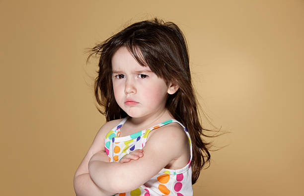 Angry or displeased little girl with long blond hair. Studio shot on yellow background.