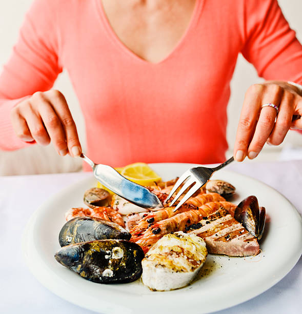 woman eating grilled seafood in a restaurant - mature woman having fish bildbanksfoton och bilder