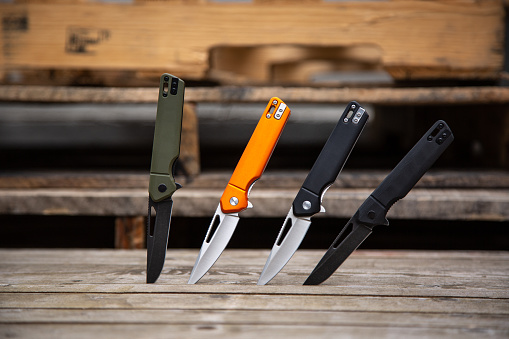 Folding penknives in different colors. Pocket knives for everyday carry. Various knives for hunting, sports and recreation. Wooden background.