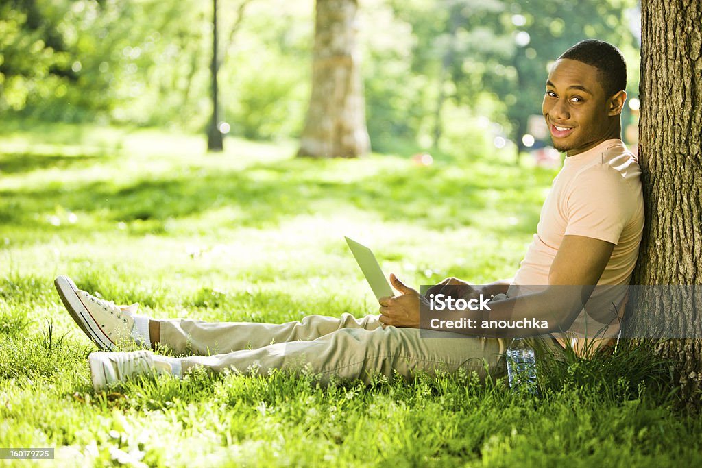 Szczęśliwy młody człowiek za pomocą laptopa w parku - Zbiór zdjęć royalty-free (20-24 lata)