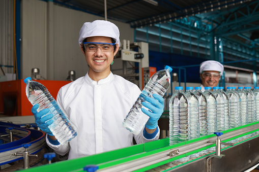 Quality control inspector specialist man checking a bottle of drinking water  on the conveyer production line in processing drinking water manufacturing