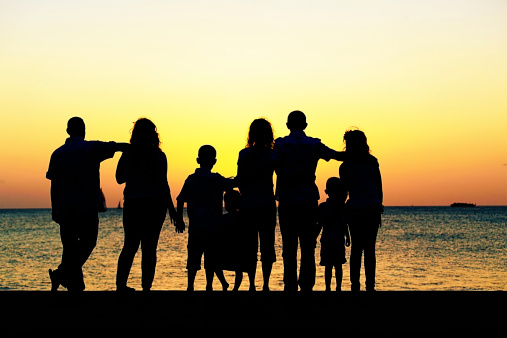 Silhouetted family of 8 watching the sun setting over the ocean. Toned image.