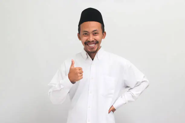 Photo of Confident young Indonesian man is giving a thumbs-up, good review, isolated on a white background