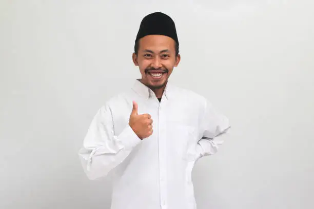 Photo of Confident young Indonesian man is giving a thumbs-up, good review, isolated on a white background