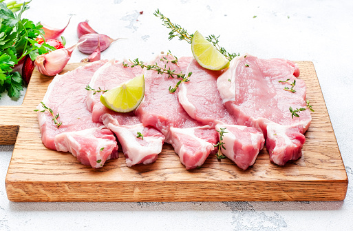 Raw pork chops, loin  on wooden cutting board prepared for cooking with garlic, thyme, spices and pepper. White kitchen table,  top view