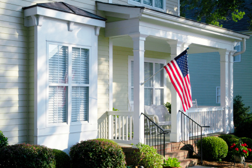 An American Flag hanging from a column on the front porch glows in the morning light as the sun rises.